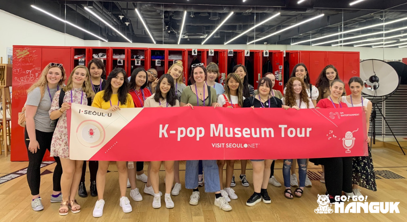 Personas que sostienen una pancarta del «K-pop Museum Tour»