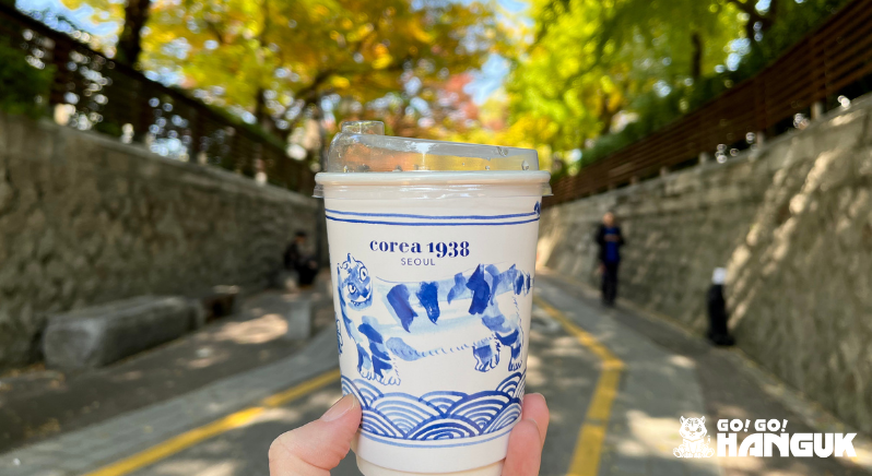 Vaso de té desechable de una marca coreana con follaje otoñal al fondo
