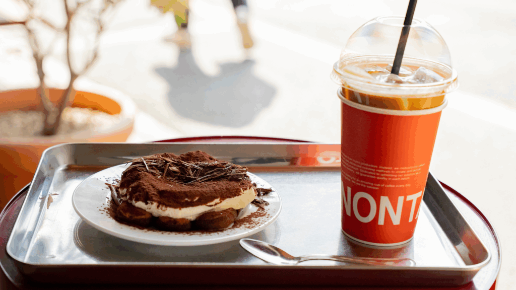 An iced Americano coffee and a tiramisu cake on a table