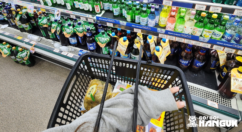 Person holding a shopping cart in front of a drink shelf